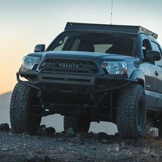 the front end of a silver toyota truck parked on top of a rocky hill with mountains in the background