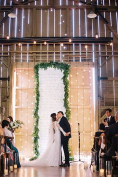 a bride and groom standing in front of a wedding arch with greenery on it