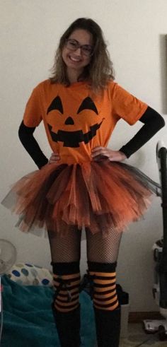 a woman in an orange shirt and black stockings is wearing a pumpkin tutu skirt