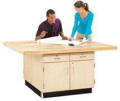 a man and woman standing at a table with papers on top of it while looking at something