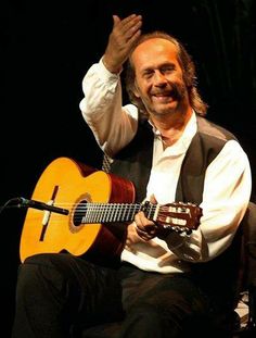 a man sitting in a chair with a guitar on his lap and hands up to the side