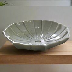 a large white bowl sitting on top of a wooden shelf next to a planter