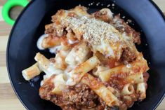 a black bowl filled with pasta and meat covered in sauce on top of a wooden table