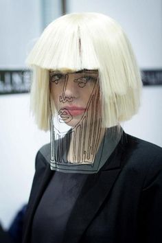 a mannequin with blonde hair wearing a black suit and white wig, looking at the camera