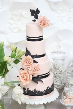 a three tiered wedding cake with pink flowers on the top and black ribbon around it