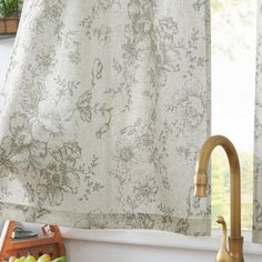 a kitchen sink with a faucet next to a window covered in floral curtains