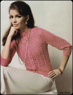 a woman wearing a pink sweater and white pants sitting on a chair with her hand on her chin