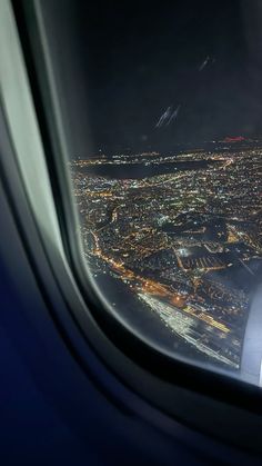 an airplane window with the view of city lights at night from inside and below it