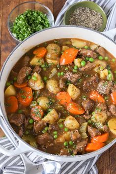 a pot full of stew with carrots, potatoes and peas on a wooden table