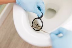 a person in blue gloves is using scissors to open a toilet bowl with the lid up