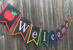 a welcome banner with an apple on it hanging from the side of a wooden fence