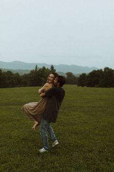 a man holding a woman in his arms while standing on top of a lush green field