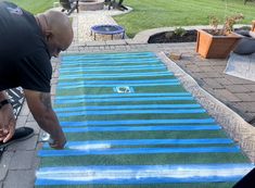 a man is painting an area with blue and green stripes on the ground in front of his house