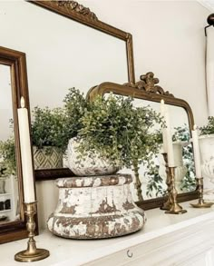 a white mantle topped with a mirror and potted plants