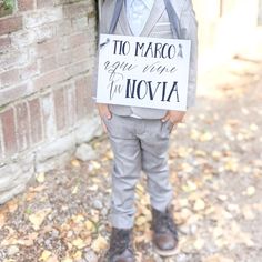 a little boy in a suit and tie holding a sign that says uncle aleganro here comes your bride