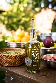 a bottle of extra virgin olive oil sitting on a table with bowls of fruit in the background