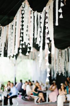 a group of people sitting and standing around tables with tassels hanging from the ceiling