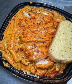 chicken parmesan and pasta in a black casserole dish with a slice of bread