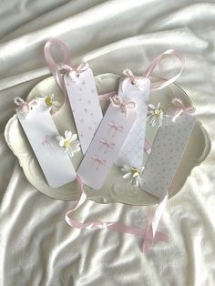 three tags on a plate with pink ribbons and daisies tied to them, sitting on a white sheet