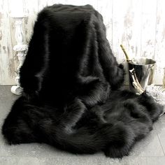 a large black furry animal laying on top of a floor next to a metal bucket