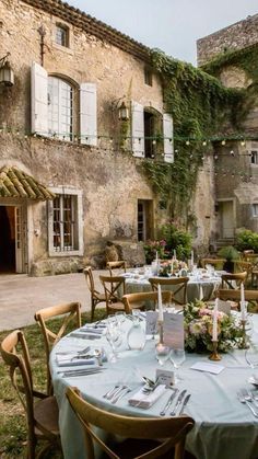 an outdoor dining area with tables and chairs in front of a stone building that has ivy growing on it