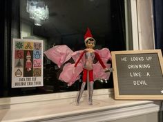 an elf is standing next to a sign that says he looks up growing like a devil