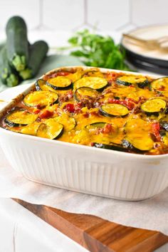 a casserole dish filled with zucchini and other vegetables on a cutting board