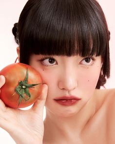 a woman holding a tomato in front of her face