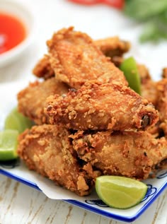 some fried food on a blue and white plate with lime wedges next to it