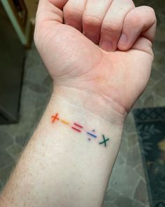 a person's arm with a cross tattoo on the left side of their wrist