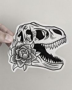 a hand holding up a sticker with a dinosaur skull and flower on the front