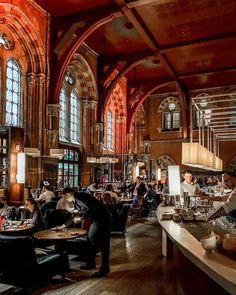 people are sitting at tables in the middle of a large room with high ceilings and arched windows