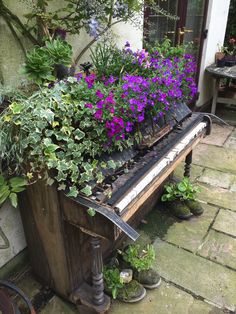 an old piano is filled with flowers and potted plants on the side of a house