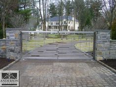 a gated driveway leading to a large house with trees in the backgroud