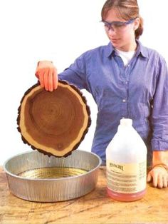 a woman is holding a piece of wood in front of a metal pan with liquid