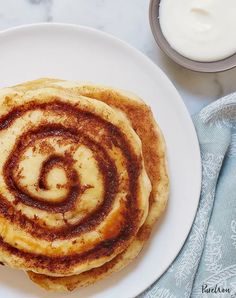 three cinnamon rolls on a white plate next to some yogurt