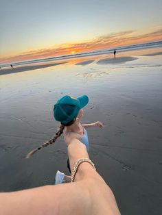 a person is holding their hand out towards the water at sunset, with two people in the background