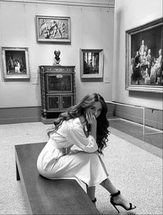 a woman is sitting on a bench in an art gallery and posing for the camera