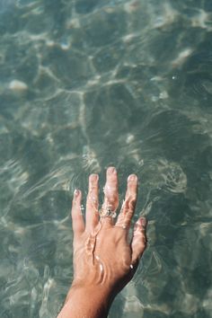 a person's hand reaching for something in the water with clear blue water behind them