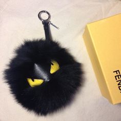 a black furry keychain with yellow eyes on it, next to a box