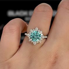 a person's hand holding a ring with a blue stone in the middle and white diamonds around it