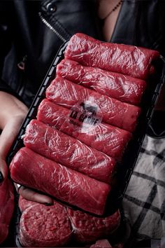 a person holding a tray with raw meat in it's hands and wearing a black leather jacket