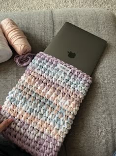 an apple laptop computer sitting on top of a gray couch next to a crocheted blanket