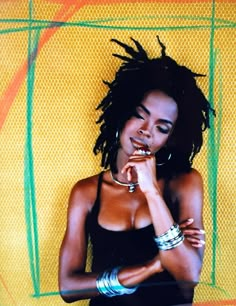 a woman with dreadlocks standing in front of a yellow and green background holding her hand to her mouth