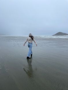 a woman is walking on the beach with her back to the camera and she has one foot in the water