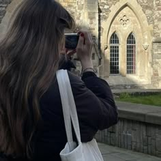 a woman taking a photo with her cell phone in front of an old stone building