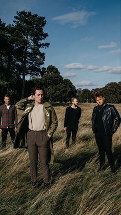 four people standing in tall grass with trees in the background and one person wearing a coat