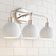 three light bathroom fixture with white tiles on the wall behind it and a round mirror above them