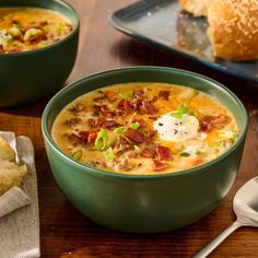 two green bowls filled with soup on top of a wooden table next to a baguette