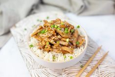 a white bowl filled with rice and meat on top of a table next to chopsticks